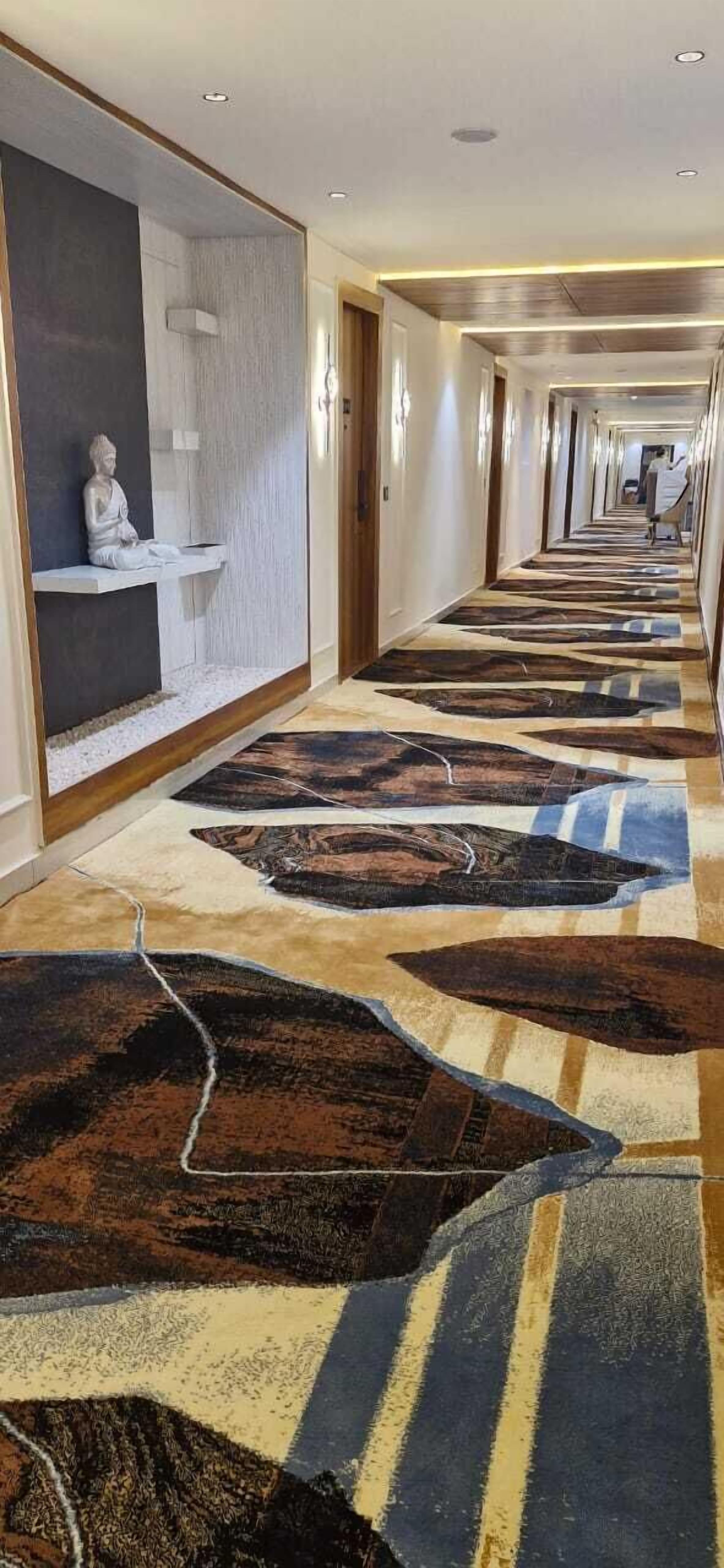 A hotel corridor with a patterned carpet, a statue on a shelf, and a long hallway with doors on both sides.