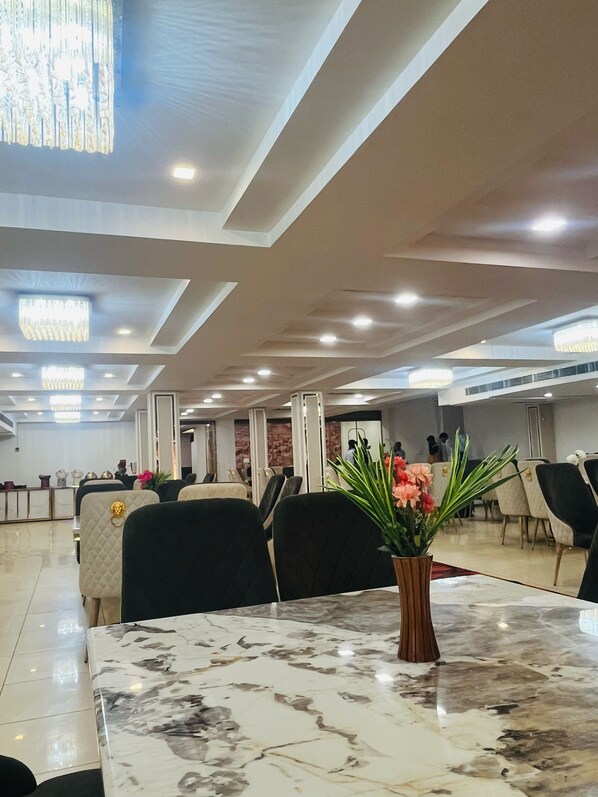 A spacious dining area with marble tables and chairs, a chandelier, and a view of the adjacent room.