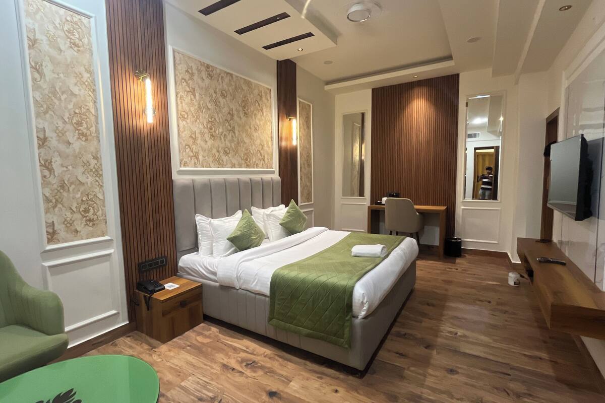 A hotel room with a large bed, a desk, a chair, a TV, and a green armchair.