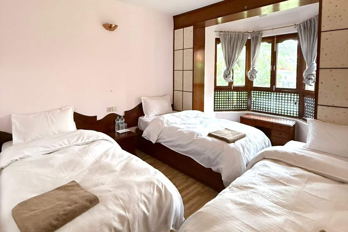 Habitación de hotel con dos camas, cabecera de madera, una mesita y una ventana con cortinas.