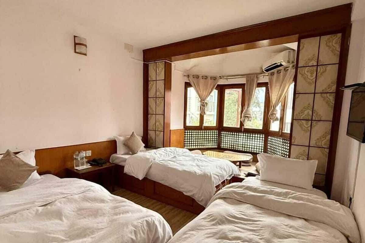 Habitación de hotel con dos camas, cabecera de madera, ventana con cortinas y aire acondicionado instalado en la pared.