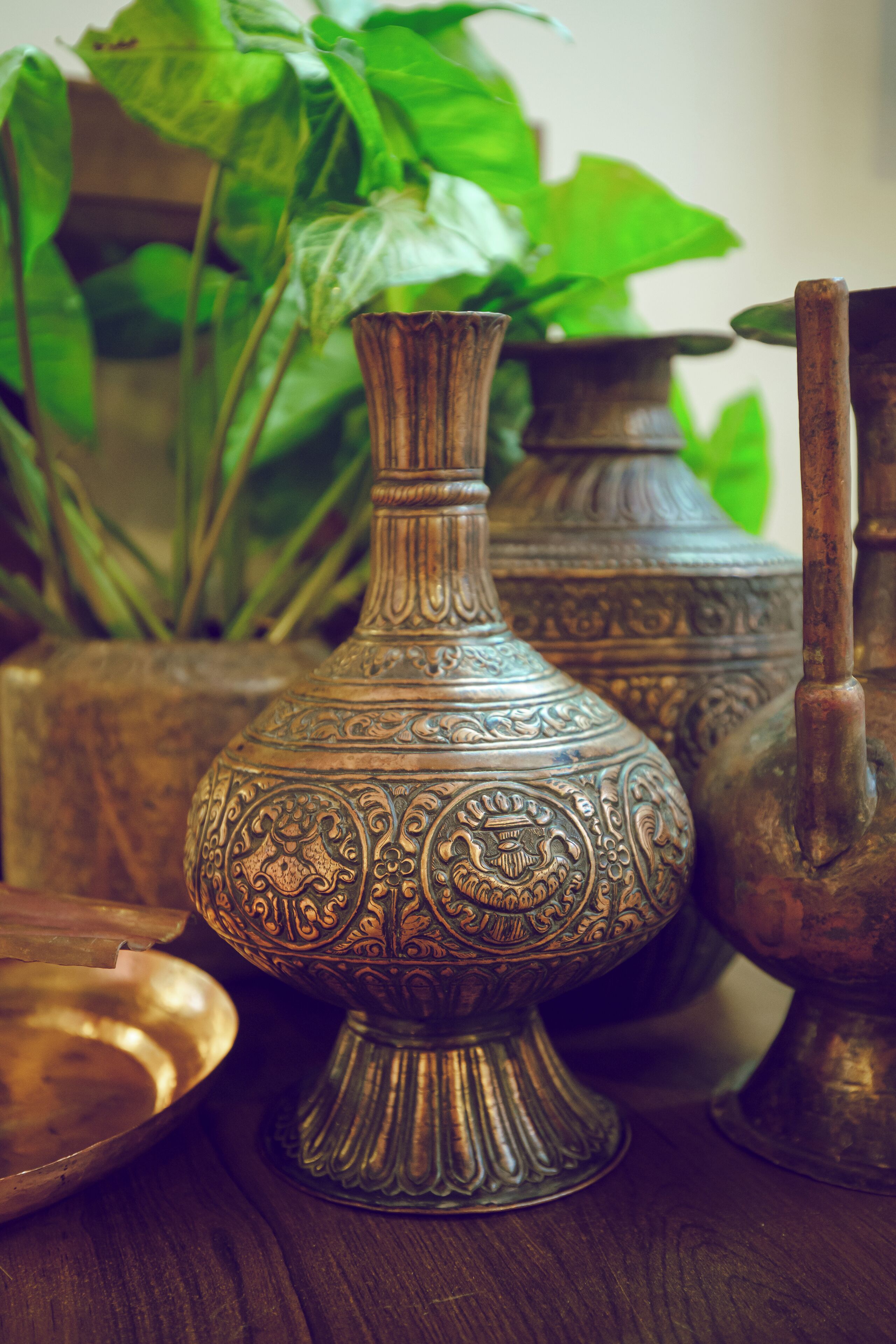 A collection of ornate metal vases and a bowl on a wooden surface.