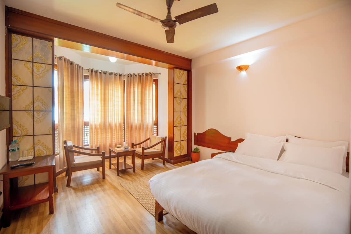 Habitación de hotel con cama, escritorio, silla, ventilador de techo y vista a través de una cortina.