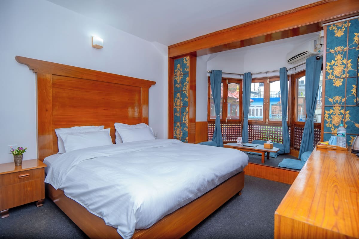 Un dormitorio ordenado con cama de madera, una mesita de noche, un pequeño rincón de estar y vistas a través de una ventana con cortinas.