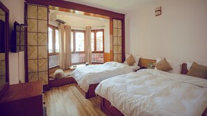 A hotel room with two beds, wooden flooring, a sliding door leading to a balcony, and a small table with a bottle. - Laavanya Inn (Pokhara)