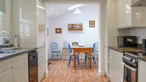 Una cocina moderna con suelo de madera, armarios blancos, una mesa de comedor con sillas y un horno empotrado.