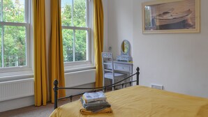 Un dormitorio con cama, cómoda, espejo y ventana con cortinas.