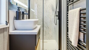 A modern bathroom with a white sink, a mirror, a shower, and a towel rack. - 2 bedroom accommodation in Chirk, near Llangollen (Chirk, near Llangollen)