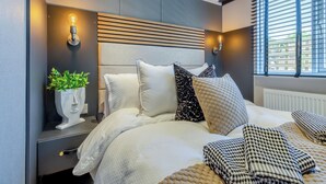 A modern bedroom with a bed, bedside tables, a wall-mounted light, and a window with blinds. - 2 bedroom accommodation in Chirk, near Llangollen (Chirk, near Llangollen)