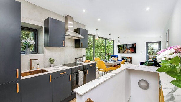 A modern kitchen with dark cabinetry, a white countertop, and a dining area with yellow chairs.