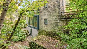 A stone building with a glass door entrance, surrounded by trees and a wooden staircase.