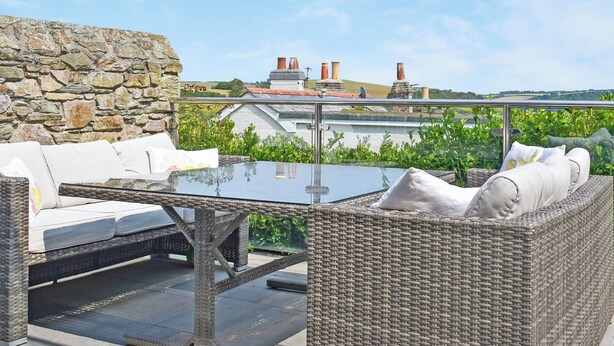 A glass-top table with wicker furniture and a stone wall backdrop. - All that Salcombe has to offer from your perfect family base. (Salcombe)