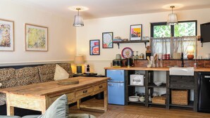 Una sala de estar acogedora con un sofá, una mesa de madera y una zona de cocina con refrigerador, fregadero y varios utensilios.