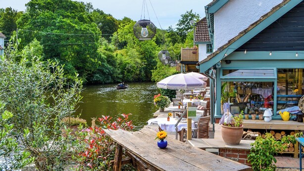 Un café junto al río con terraza al aire libre, una plataforma de madera y vistas del río.
