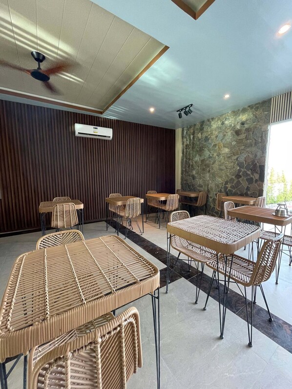 A modern indoor dining area with wicker furniture, a ceiling fan, and a stone wall.