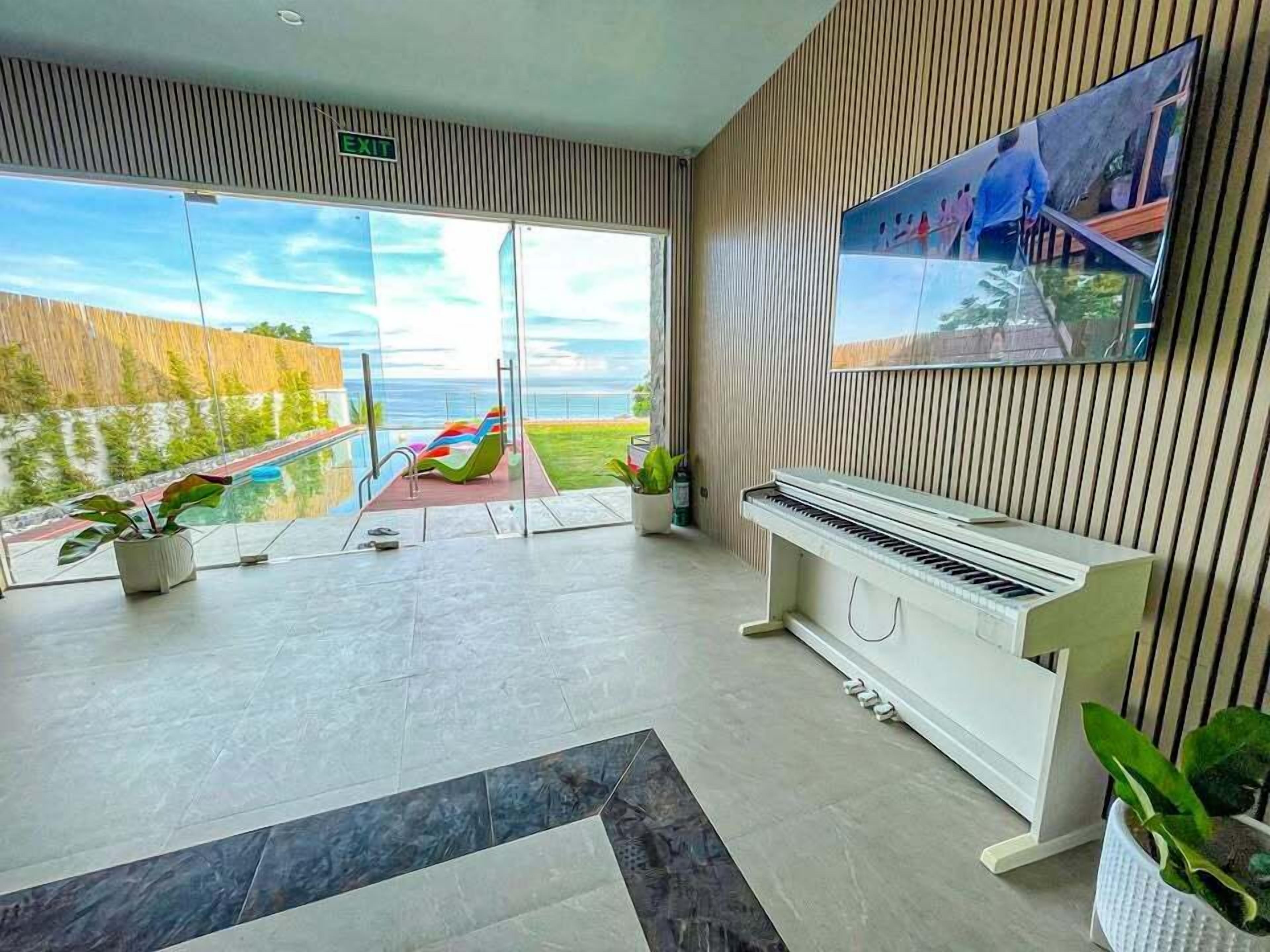 Una habitación moderna con un piano, un televisor grande y vista al océano.