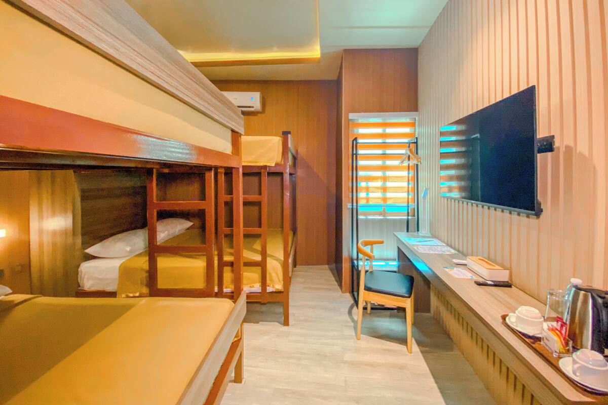 Ein Hotelzimmer mit Etagenbetten, einem Schreibtisch mit Stuhl, einem Fernseher und einem Fenster mit Jalousien.