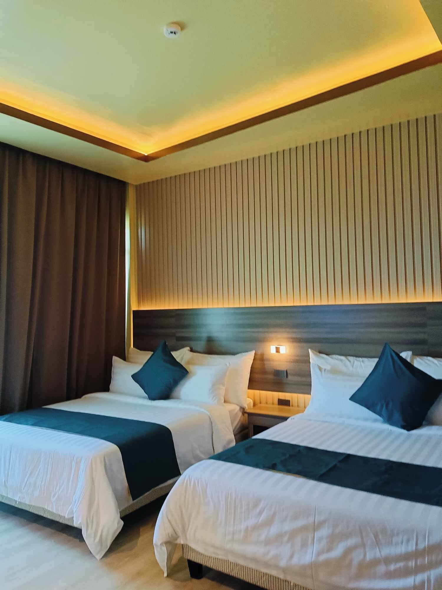 A hotel room with two beds, each with white bedding and dark blue pillows. The room has a wooden headboard and a striped wall.