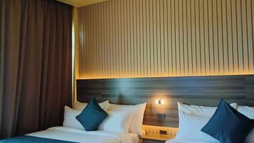 A hotel room with two beds, each with white bedding and dark blue pillows. The room has a wooden headboard and a striped wall.