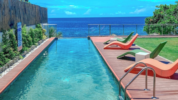 Una piscina con agua cristalina, muelle de madera y sillones de descanso.