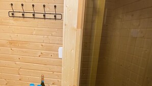 A wooden room with a shelf holding towels and a bottle of wine.