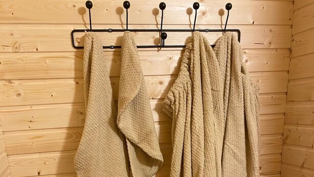 A wooden sauna room with towels hanging on hooks and a shelf with folded towels.