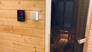 A wooden cabin interior with a digital thermostat, a light switch, and a glass door leading to a seating area.