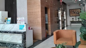 Un lobby moderno con mostrador de recepción, zona de estar y una planta grande.