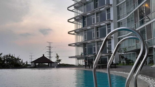 Una piscina con barandillas metálicas, un pabellón y un edificio moderno de varios pisos con amplias ventanas.