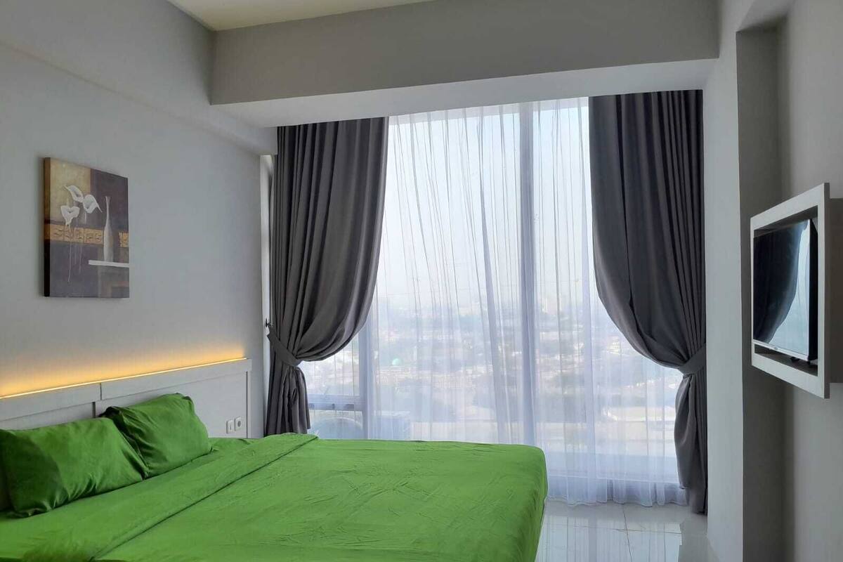A hotel room with a bed, a TV, and a window with curtains.