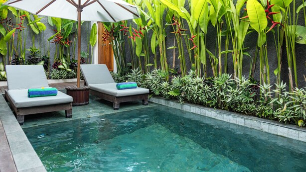 A pool area with lounge chairs, a wooden deck, and tropical plants. - Jenna Villa by GenuineHost (Ubud)