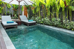 Un área de piscina con sillones de descanso, una terraza de madera y plantas tropicales.