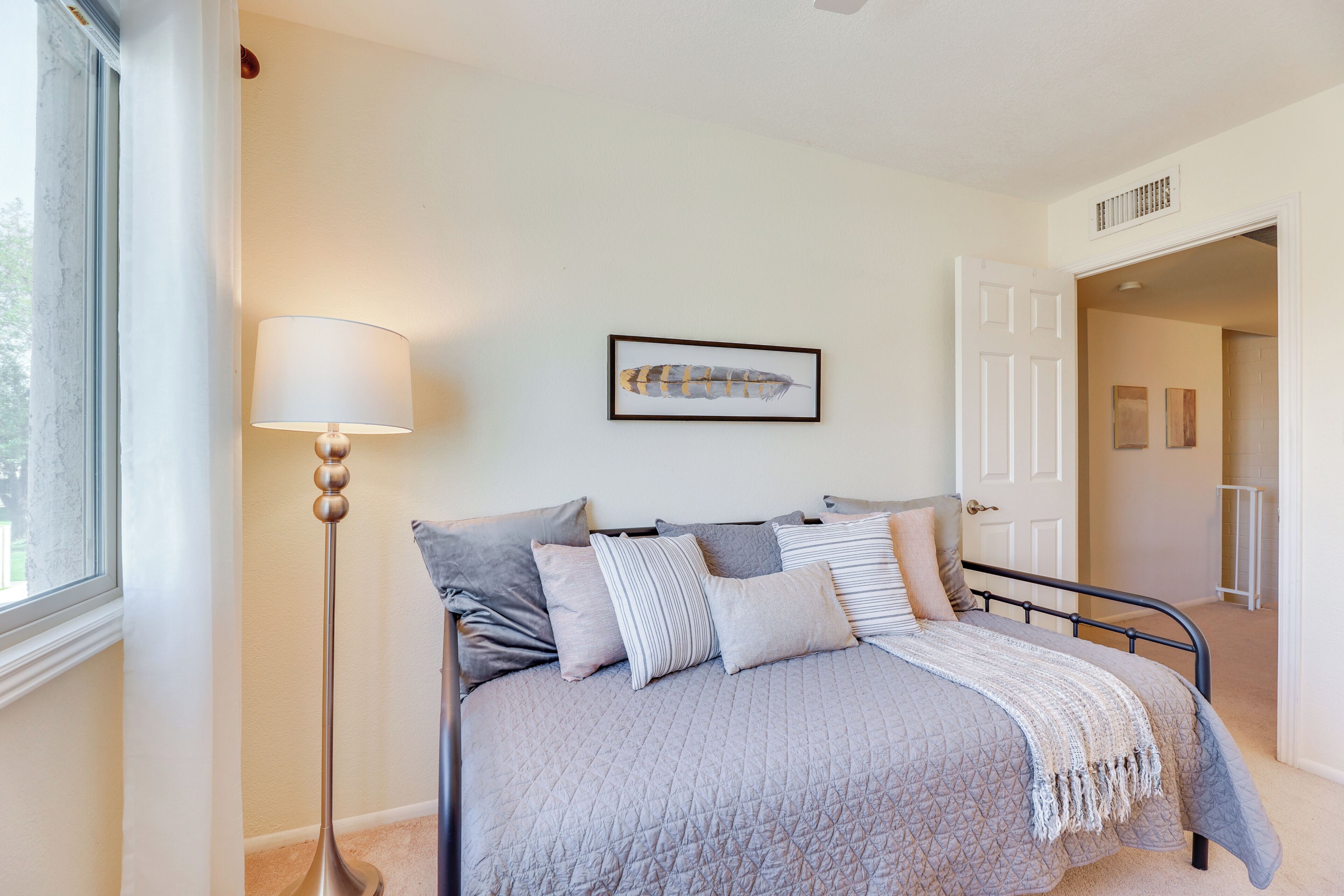 Un dormitorio con cama, almohadas, una lámpara de pie y un cuadro en la pared.
