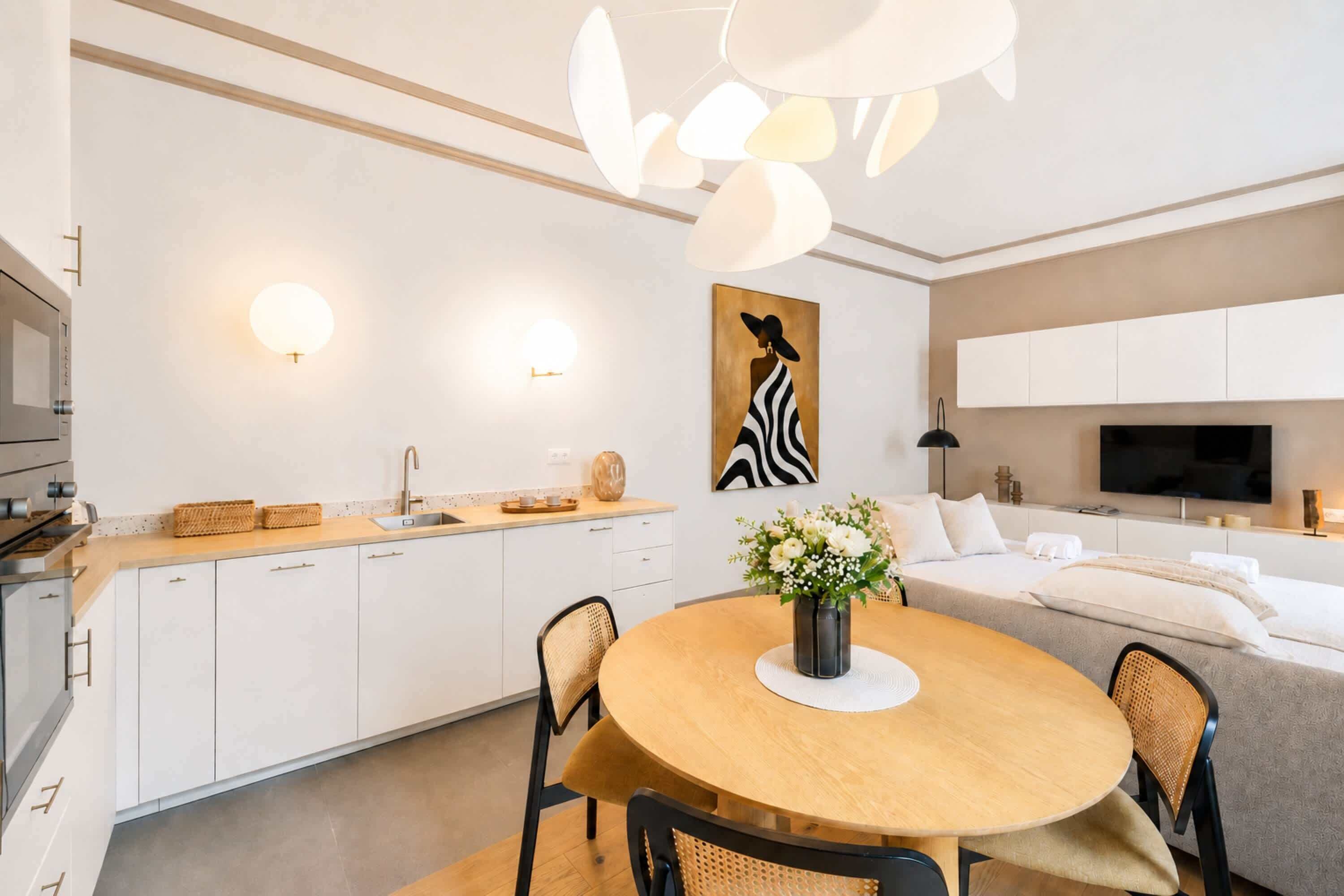 Une cuisine moderne avec des meubles blancs, une table à manger avec des chaises, un vase de fleurs et un tableau accroché au mur.