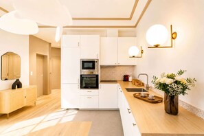 Une cuisine moderne avec des meubles blancs, un four encastré, un four à micro-ondes et une machine à café.