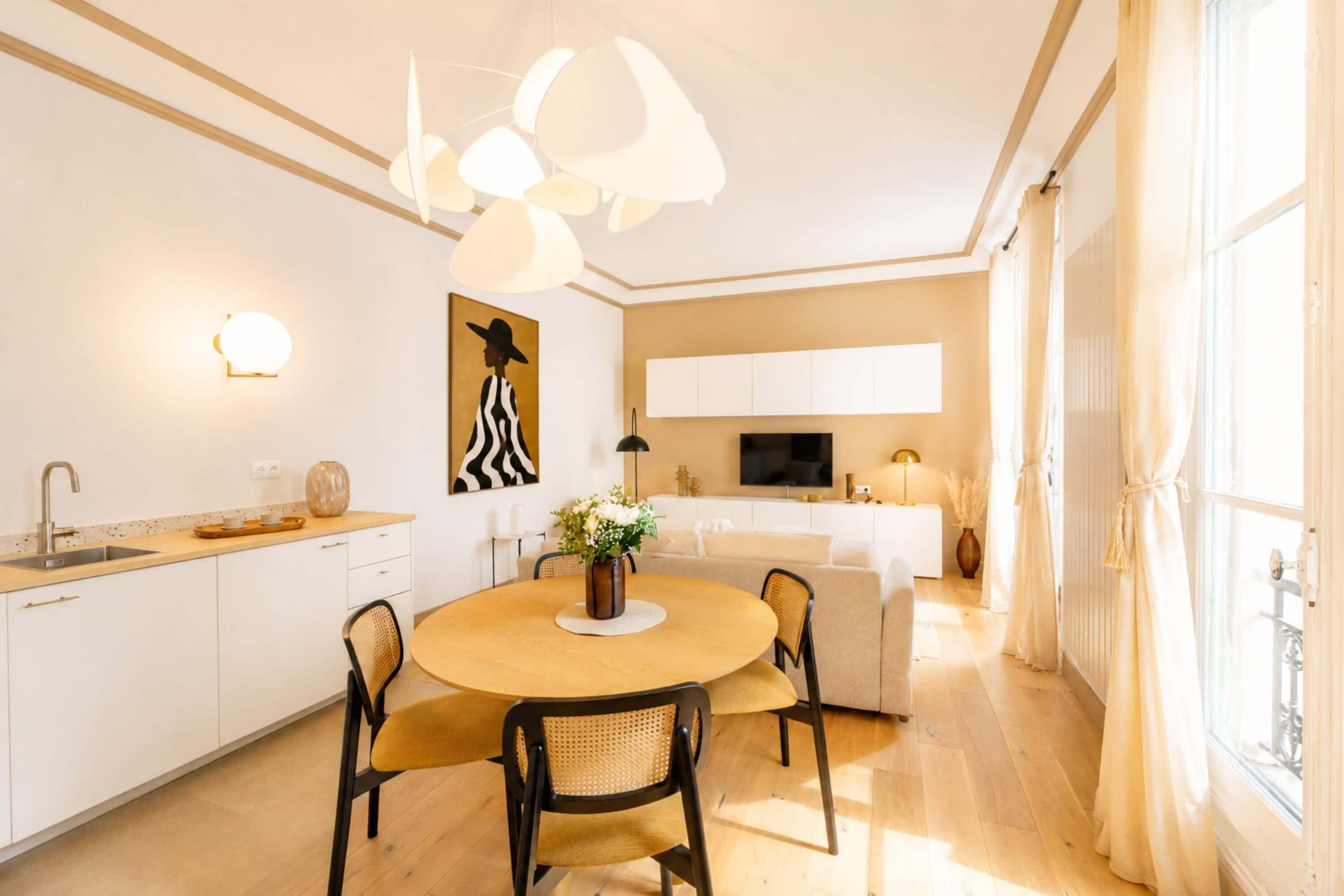 A modern kitchen with white cabinets, a dining area with a round table and chairs, and a large window with curtains.