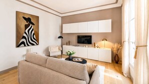 Een moderne woonkamer met een bank, een flatscreen televisie, een wit kastje en een schilderij aan de muur.