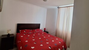 A bedroom with a bed, a nightstand, a lamp, and a window with curtains.