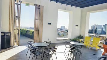 Una terraza en la azotea con una mesa redonda y sillas, un cubo de basura y vistas panorámicas de la ciudad.