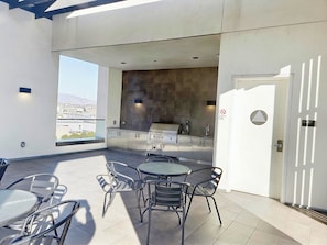 A rooftop patio with a round table and chairs, a built-in grill, and a view of the city.
