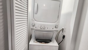 A compact, white laundry room with a front-loading washing machine and dryer, a control panel with various settings, and a power outlet.