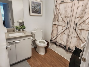 A bathroom with a wooden door, a sink, a toilet, and a framed artwork on the wall.