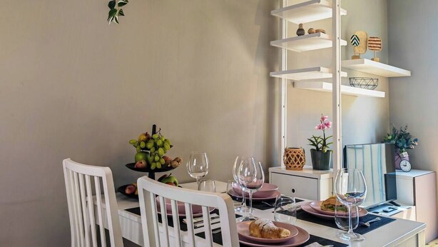 Un comedor con una mesa blanca dispuesta para dos personas, una planta colgando del techo y un aparador blanco con objetos decorativos.