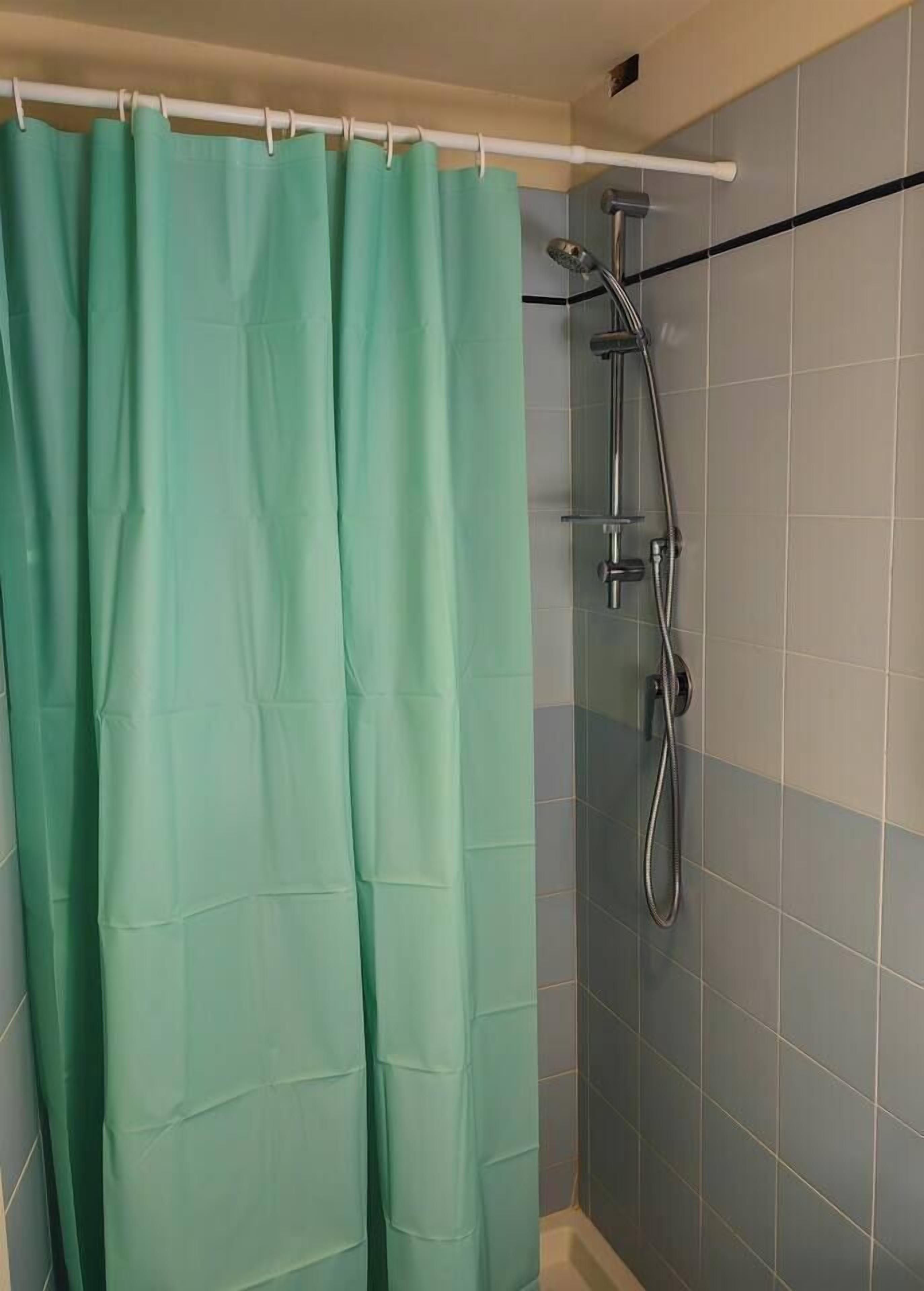 A bathroom with a green shower curtain, a handheld showerhead, and a wall-mounted faucet.