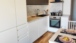 Cocina compacta con armarios blancos, encimera de madera, horno integrado y comedor con mesa lista para dos personas.