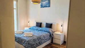 Un dormitorio con cama, mesitas de noche, una lámpara colgante y un cuadro en la pared.