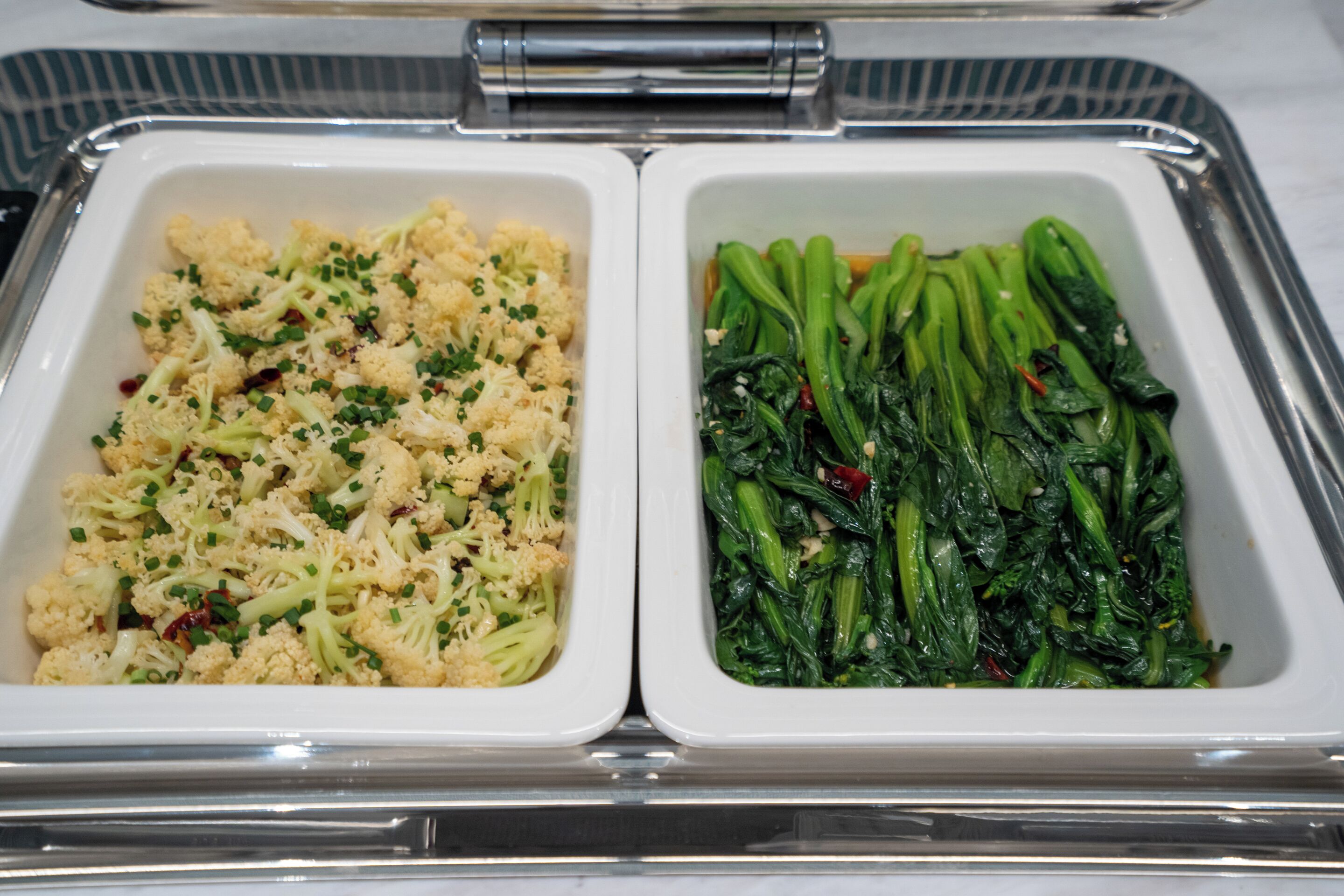 Un servicio de comida con dos compartimentos, uno con coliflor y el otro con verduras verdes.