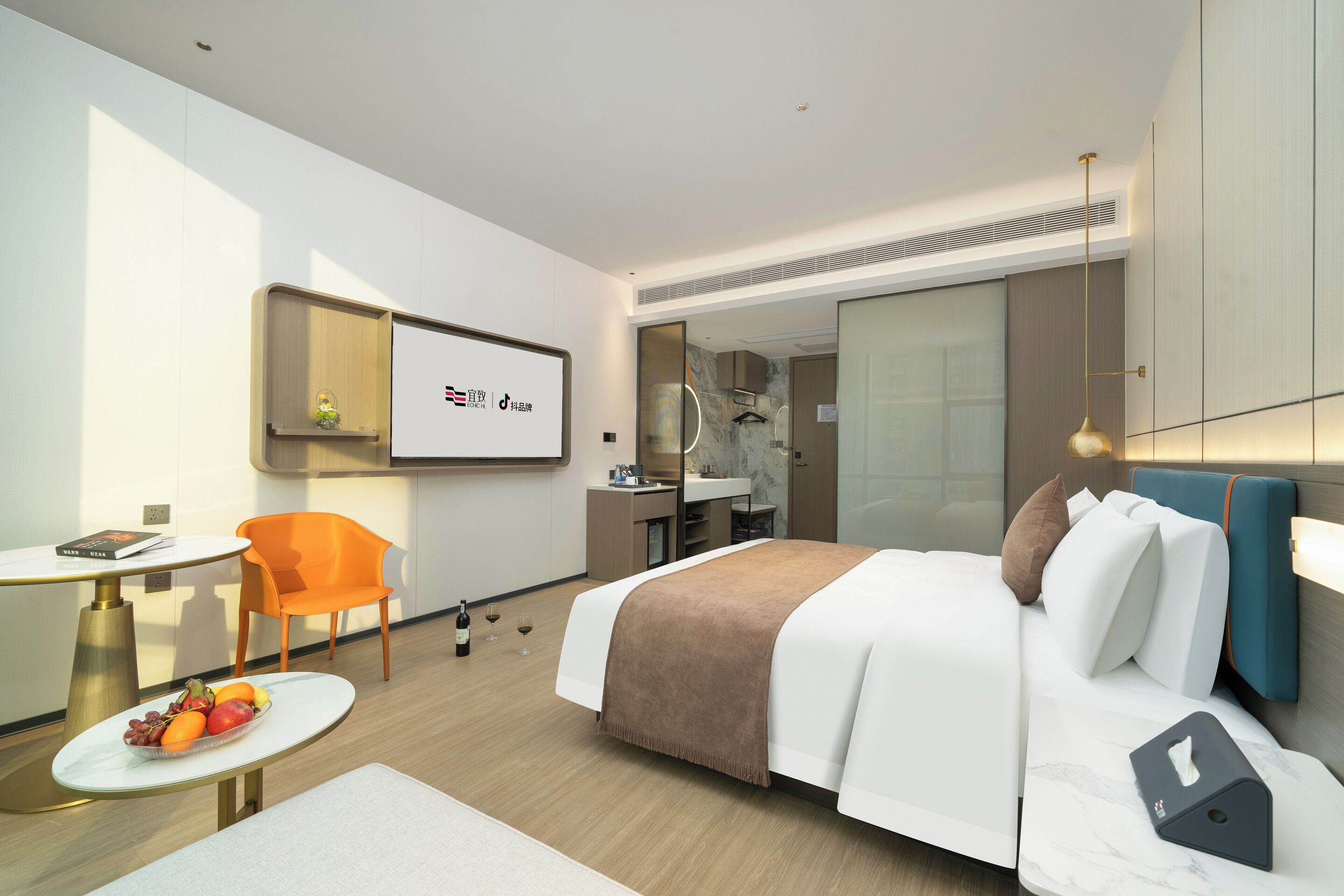 A modern hotel room with a bed, bedside table, chair, and a small desk with a mirror.