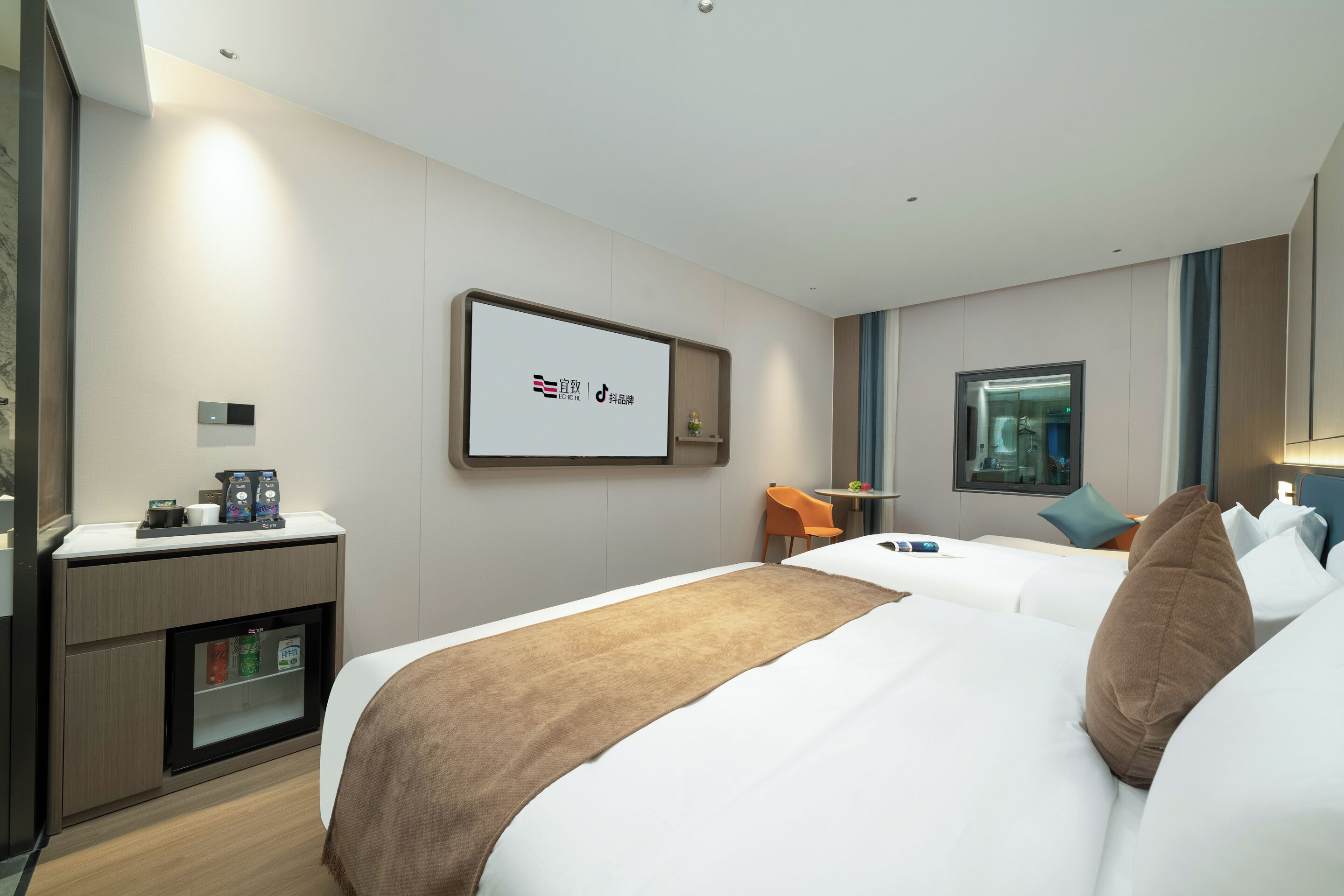A hotel room with a bed, a desk with a coffee maker, a small table with a chair, and a wall-mounted TV.