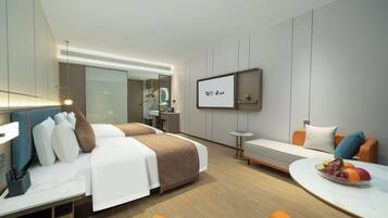 Habitación de hotel moderna con cama, escritorio, zona de estar y una pantalla de televisión mostrando un logotipo.